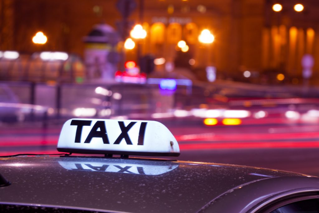 Shining Taxi inscription against passing cars on night street of big city